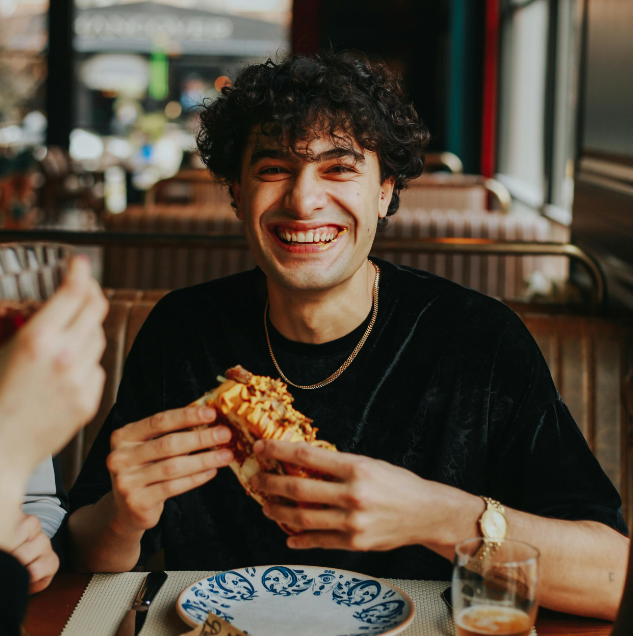 Young man eating a sandwich at a restaurant while smiling